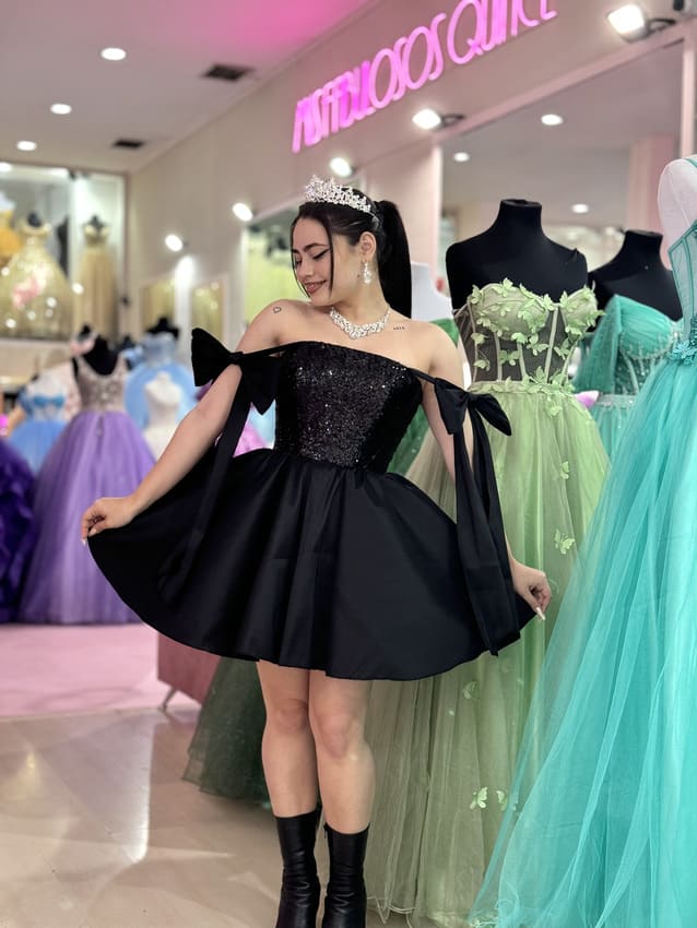 Vestido de 15 corto negro con corset brillante, falda amplia tipo campana y mangas caídas con lazos, en tienda de vestidos de fiesta.