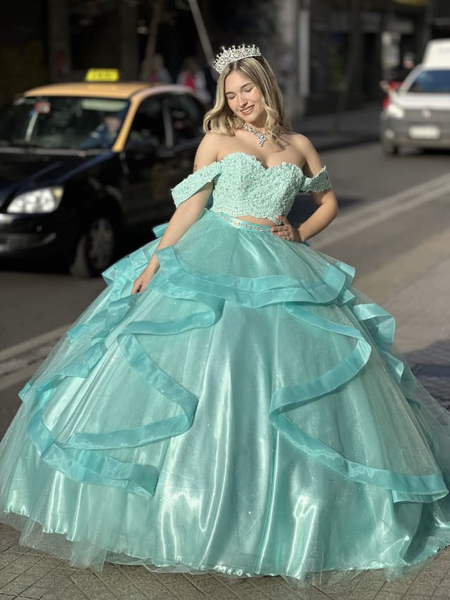 Vestido de 15 verde agua estilo princesa con corset off shoulder bordado y falda amplia con volados de tul, lucido en exterior urbano.