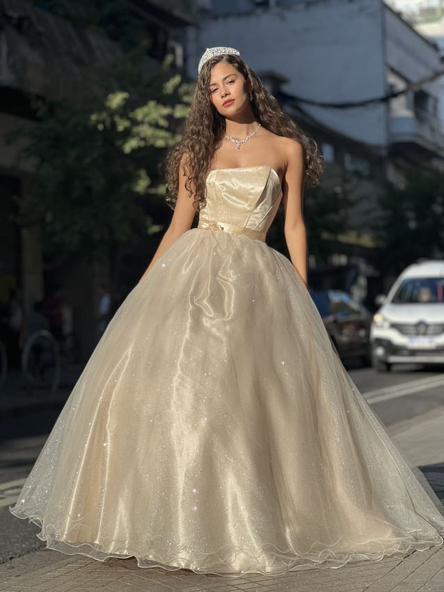 Vestido de quince color champagne con falda voluminosa de tul brillante y corset strapless, usado por una joven con tiara en una calle urbana.