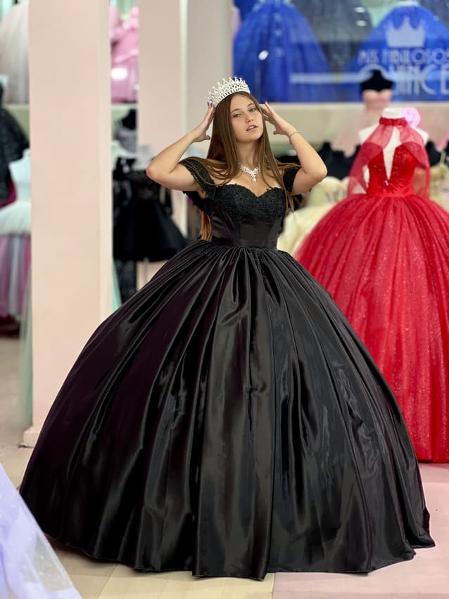 Vestido de quince negro con falda amplia satinada y corset con encaje, usado por una joven con tiara en una tienda de vestidos.