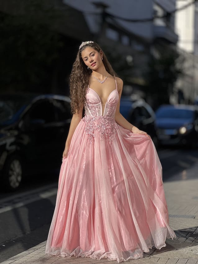Vestido de quince rosa con falda de tul voluminosa y corset bordado, usado por una joven de pie en una calle urbana.