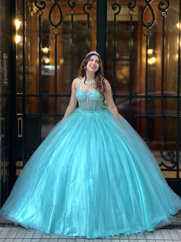 Vestido de quince celeste estilo princesa con corset bordado con breteles y falda amplia de tul, lucido en entrada elegante con rejas de fondo.